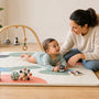 Parent supervising an awake baby during tummy time on a firm floor play mat