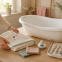 Parent preparing a dry infant bath tub with a hooded towel, washcloths, bath thermometer and baby grooming kit