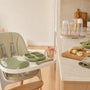 Parent preparing a high chair with a silicone feeding set, bib, snack cup and age-appropriate first foods