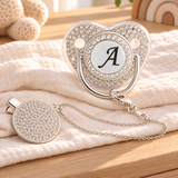 Silver initial A pacifier and crystal-style clip styled on ivory muslin in a sunlit nursery