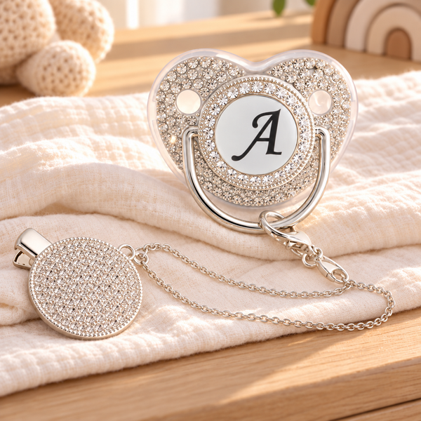Silver initial A pacifier and crystal-style clip styled on ivory muslin in a sunlit nursery